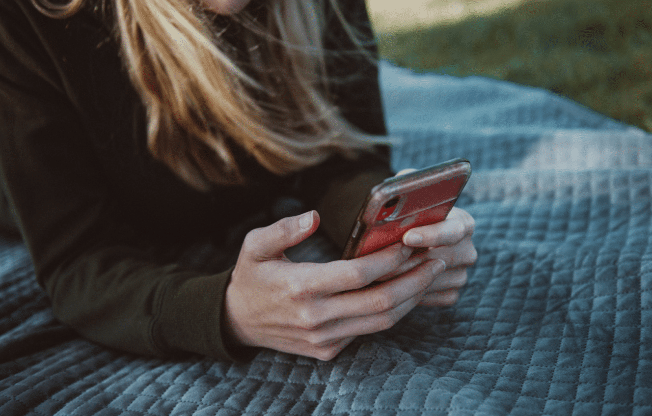 Kvinna ligger på en filt i en park och använder smartphone