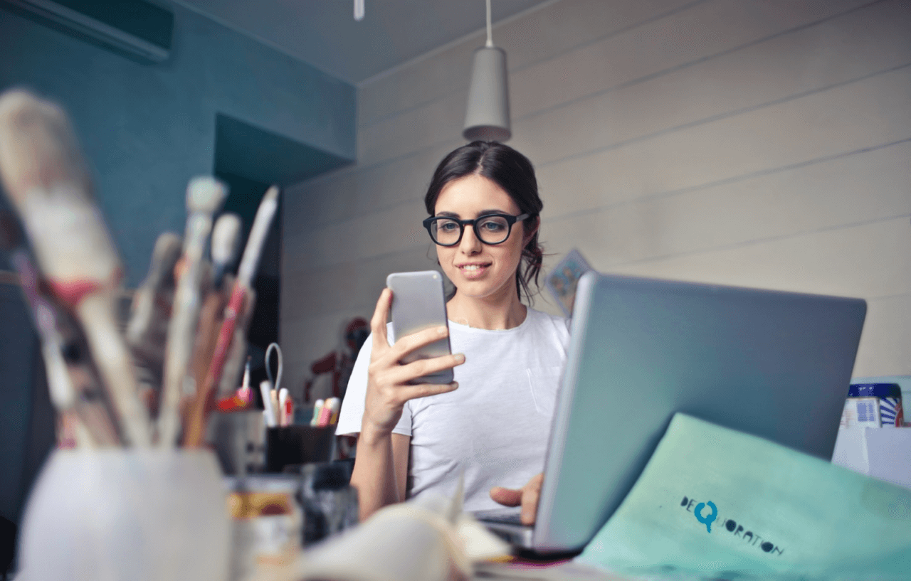 Ung kvinna använder sociala medier på mobil och dator samtidigt