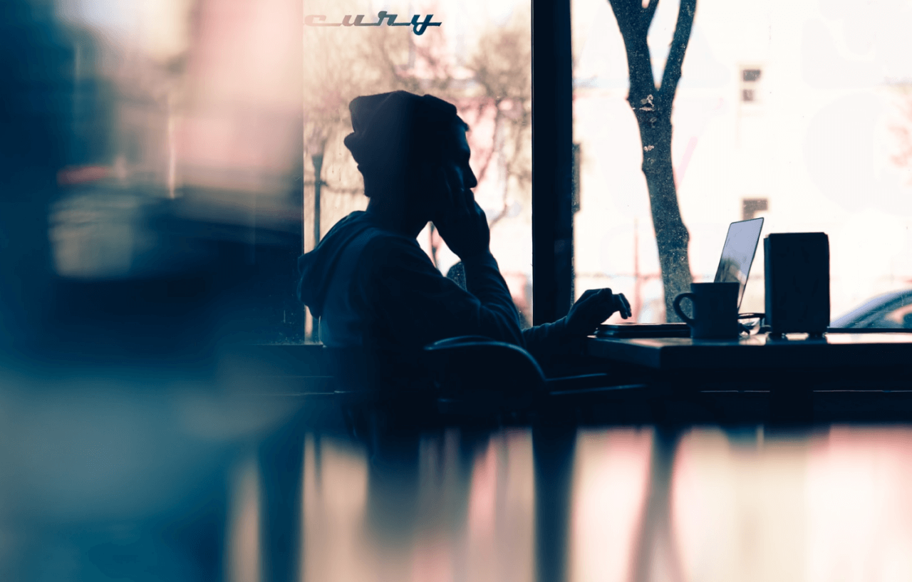 Ung man pratar i telefon medan han använder datorn på ett kafé