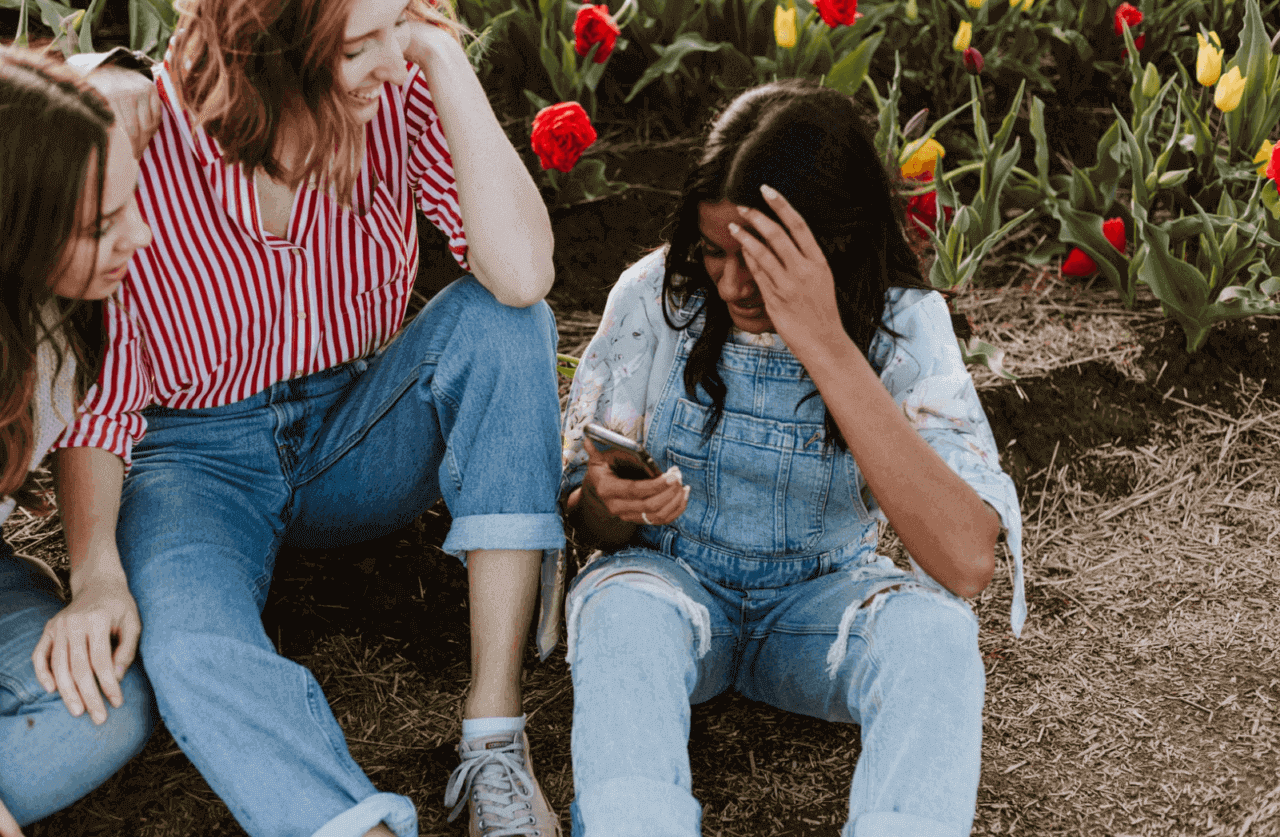 Ung kvinna skriver på telefon med hennes vänner i ett blomfält