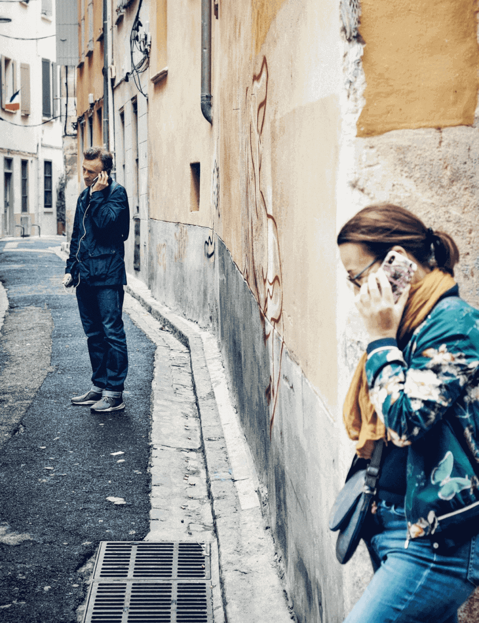 En kvinna och en man är i varsitt telefonsamtal i en gränd