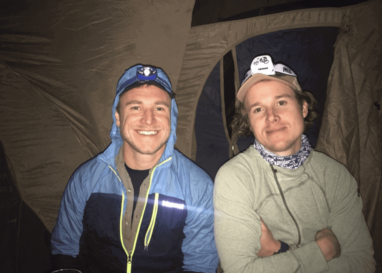 Två killar med huvudlampor framför ett tält ler mot kameran